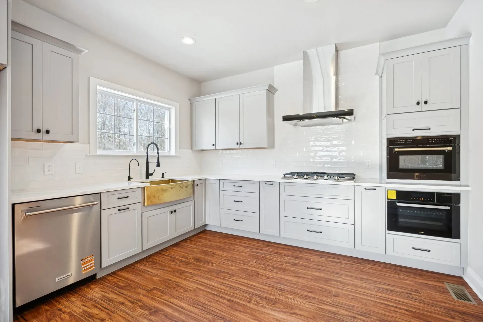 Bright white kitchen with wood floors, gray cabinets, stainless appliances, and a window over the sink