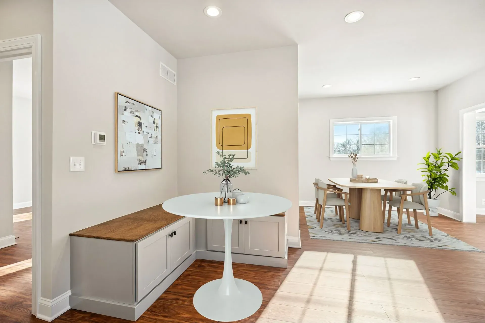 Bright open dining nook with white table, wooden benches, wall art, and sunlight on hardwood floor