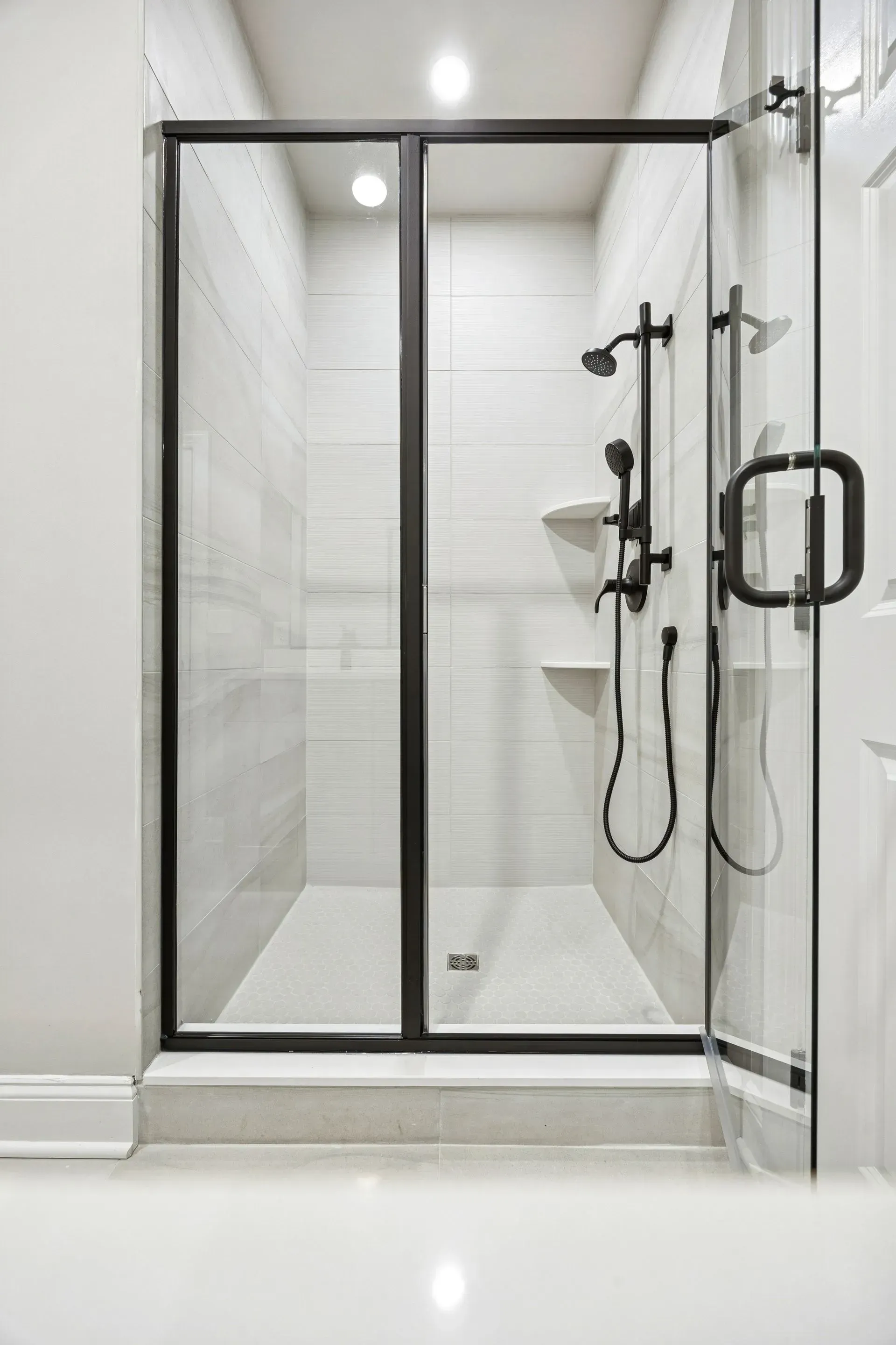 Modern glass shower stall with white tile, black trim, and wall-mounted shower fixtures