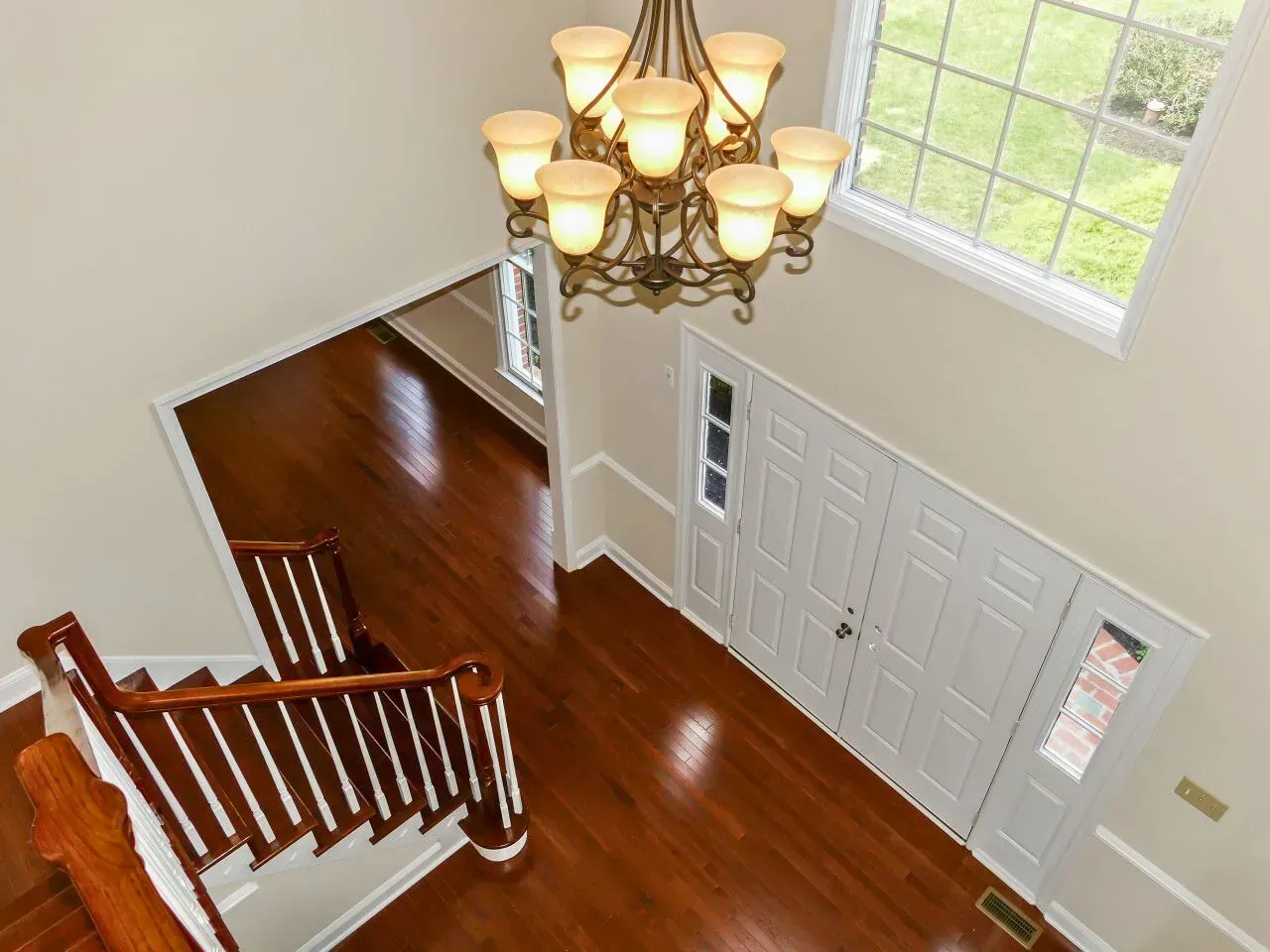 Top-down view of a foyer with a wood staircase, chandelier, white front doors, and hardwood floors.