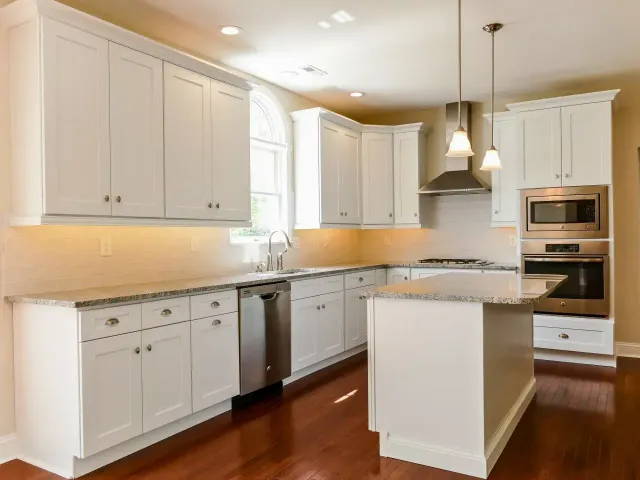 Bright white kitchen with island, stainless appliances, pendant lights, and hardwood floors