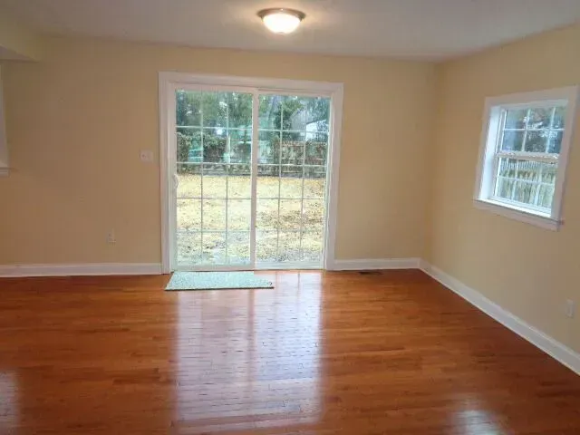 Empty beige room with hardwood floor and sliding glass door to a patio