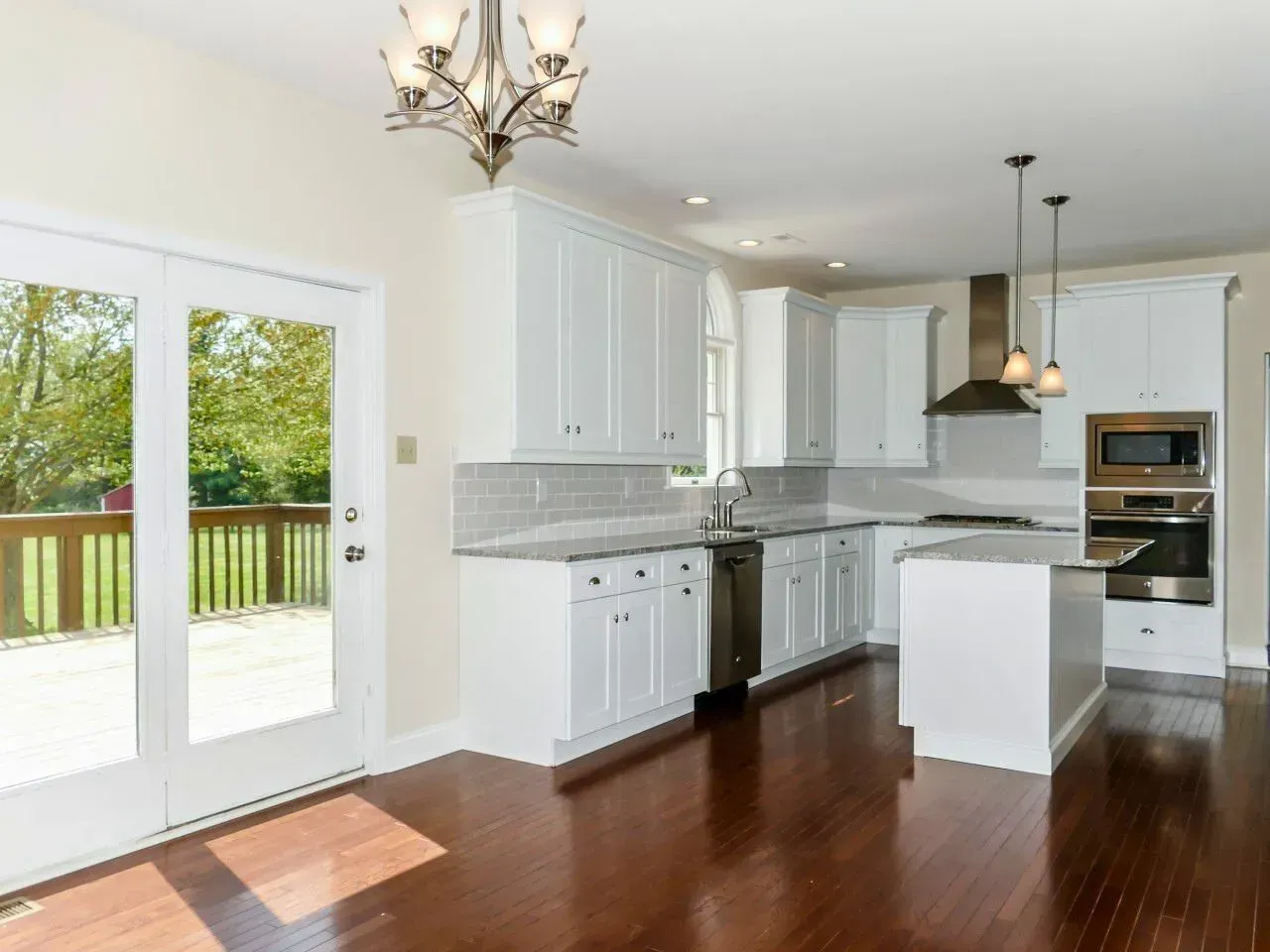 Bright modern kitchen with white cabinets, dark wood floors, island, and glass doors to a deck