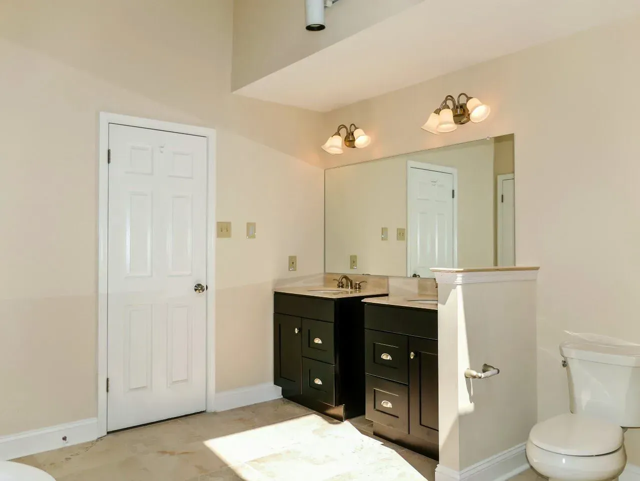 Empty bathroom with double vanity, large mirror, and toilet beside a half wall