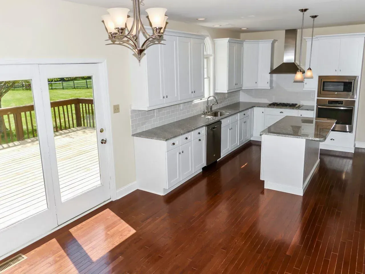 Bright kitchen with white cabinets, gray countertops, and hardwood floors beside a sunlit deck door