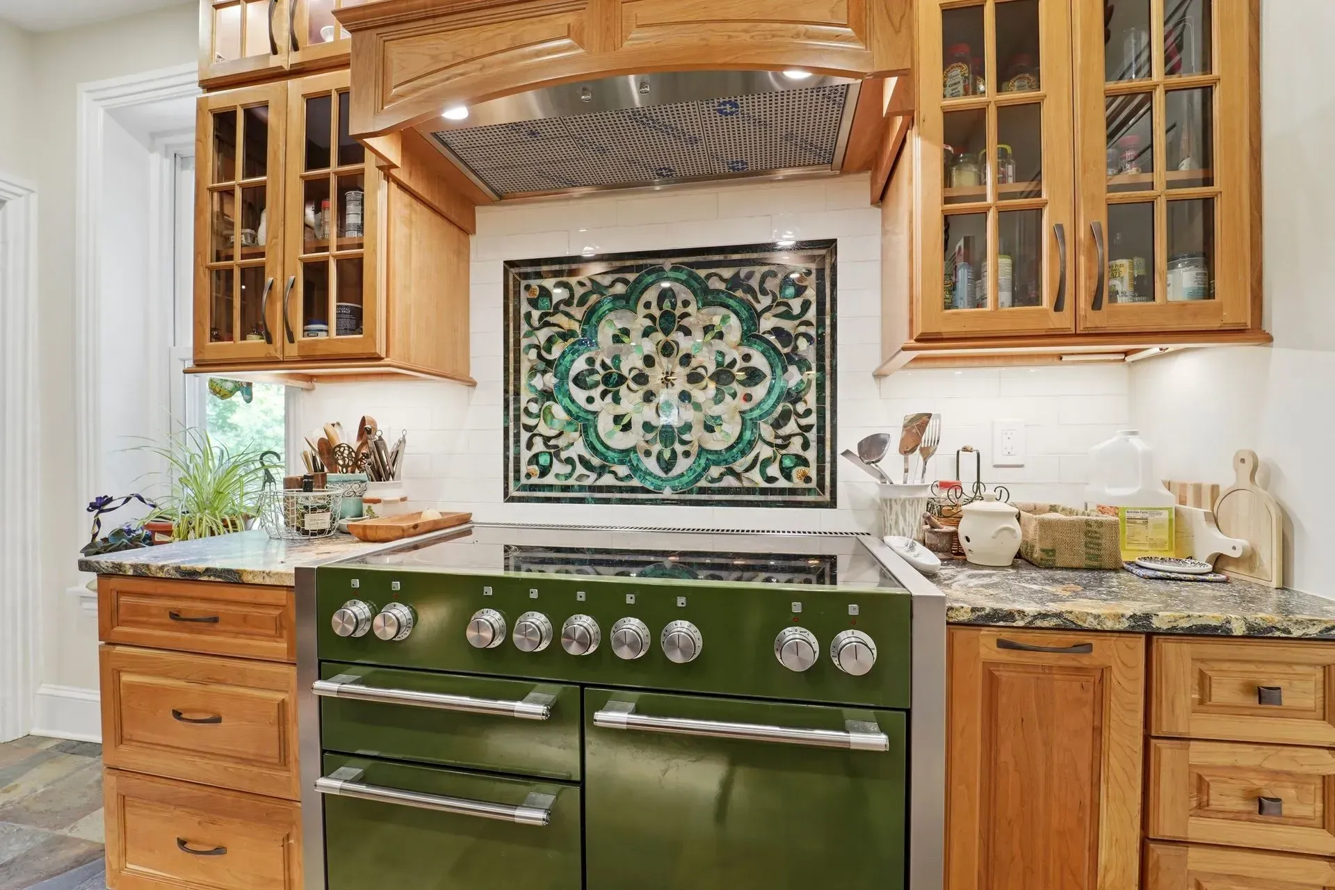 Green vintage stove in a bright kitchen with wood cabinets and patterned tile backsplash