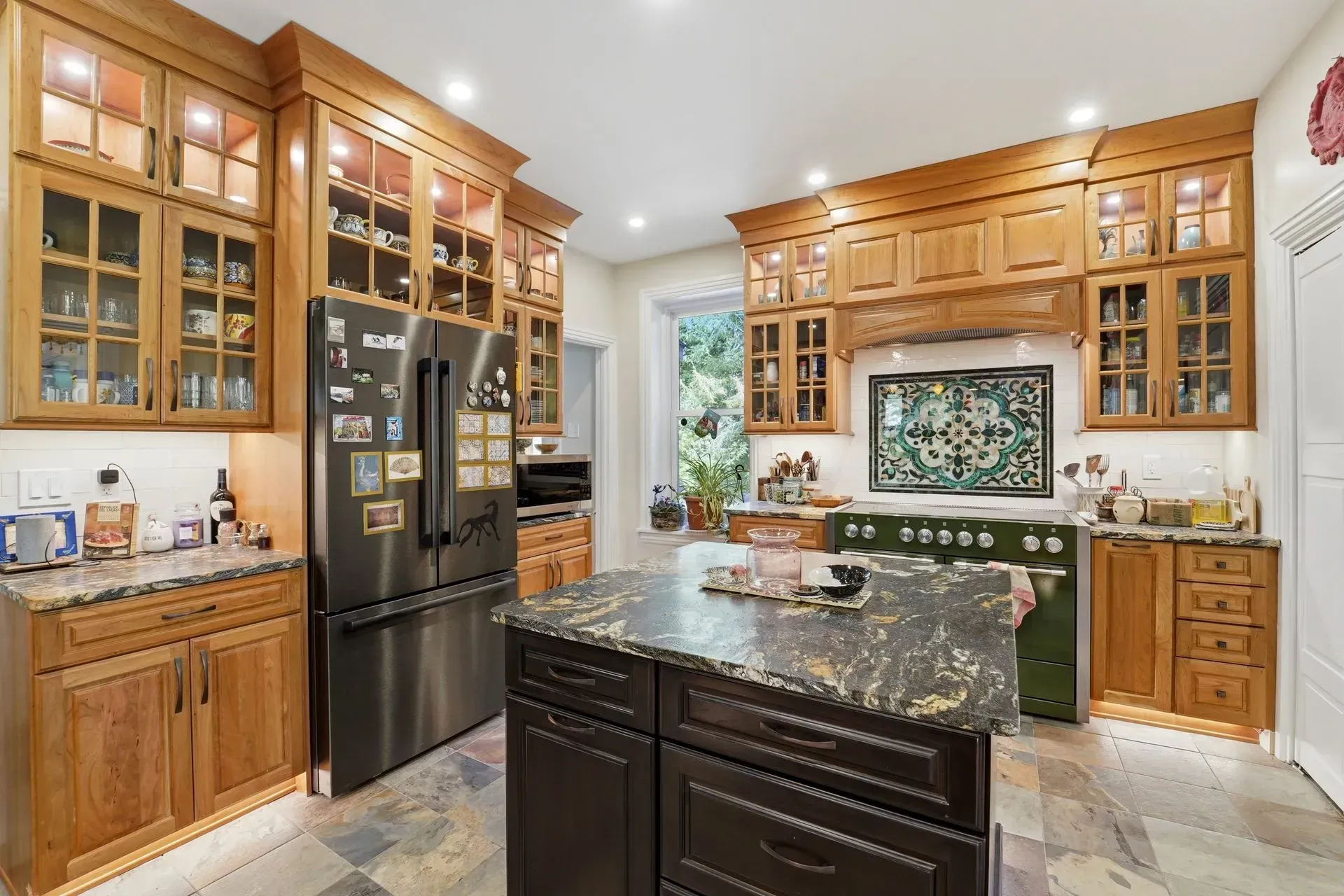 Bright kitchen with wooden cabinets, black refrigerator, marble island, and decorative backsplash