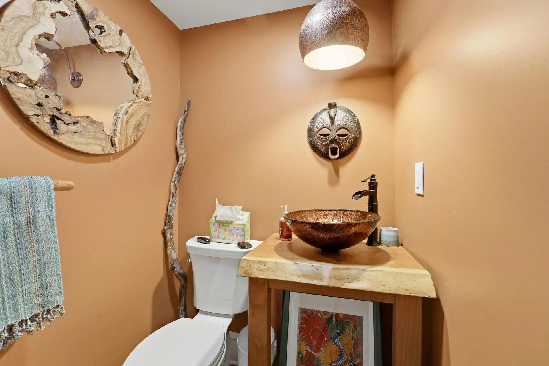 Small rustic bathroom with tan walls, copper sink, white toilet, and decorative mirrors and lighting.