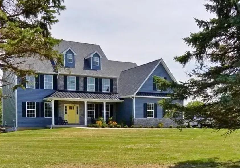 Blue two-story suburban house with yellow front door and large lawn, framed by trees