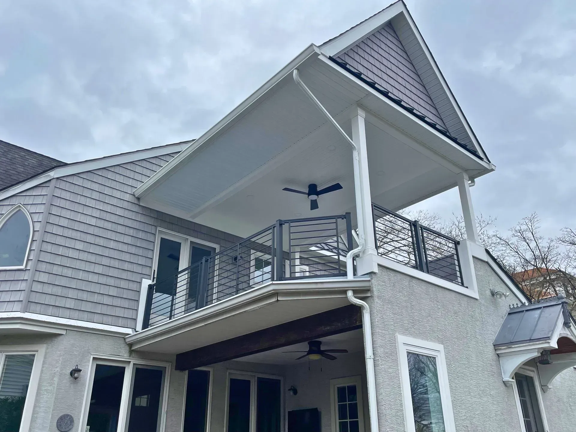 Two-story gray house with covered balcony and sloped roof under cloudy sky