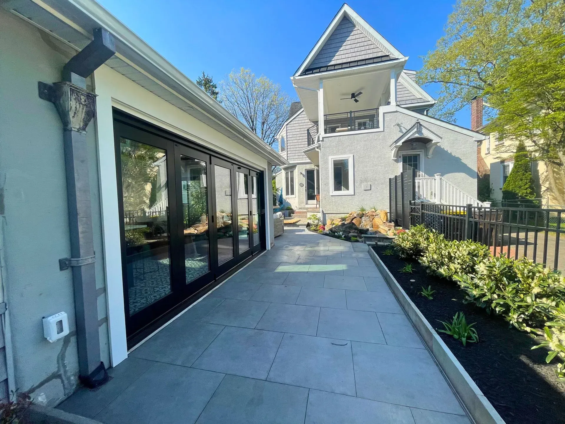Side walkway beside a white house with large windows, concrete path, and a landscaped garden under clear blue sky