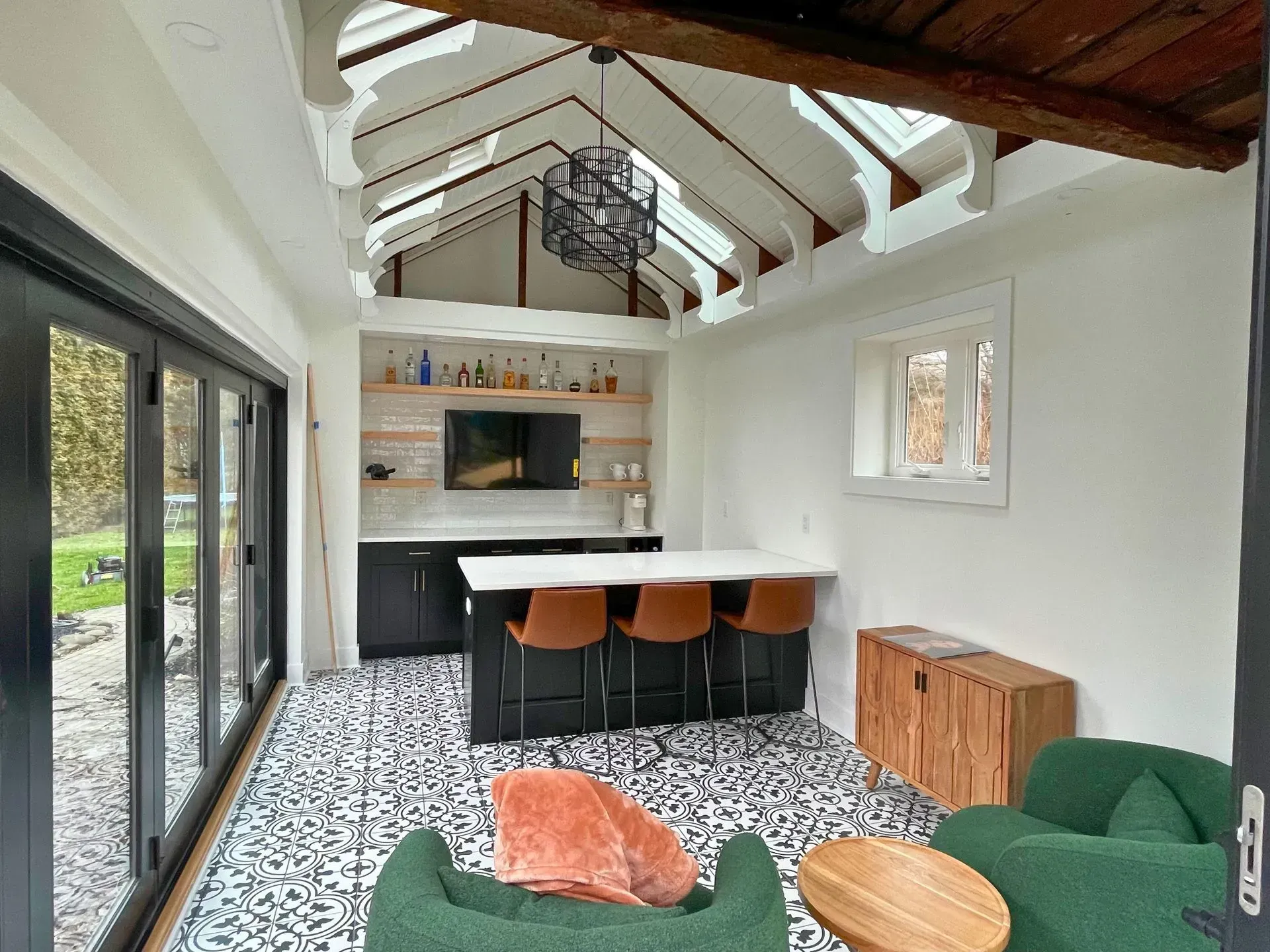 Bright modern living room with skylight, bar stools, green sofa, and black-and-white patterned floor