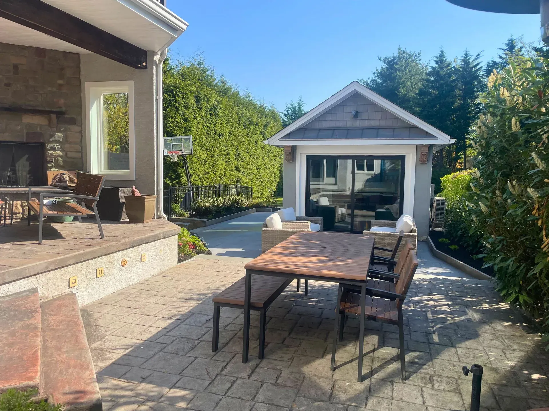 Backyard patio with dining table and chairs leading to a small garden shed under a blue sky
