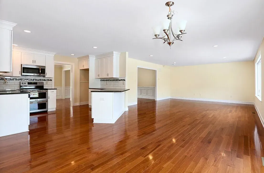 Empty open-plan kitchen and living room with hardwood floors, white walls, and chandelier lighting