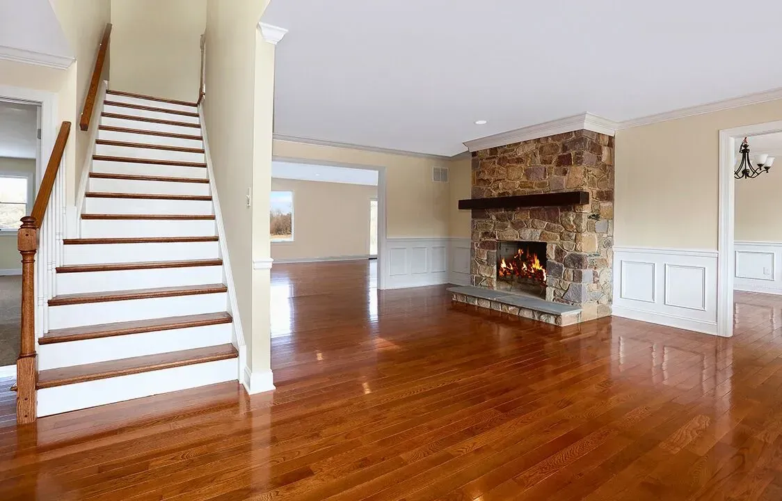 Bright living room with hardwood floors, staircase, and stone fireplace with fire burning