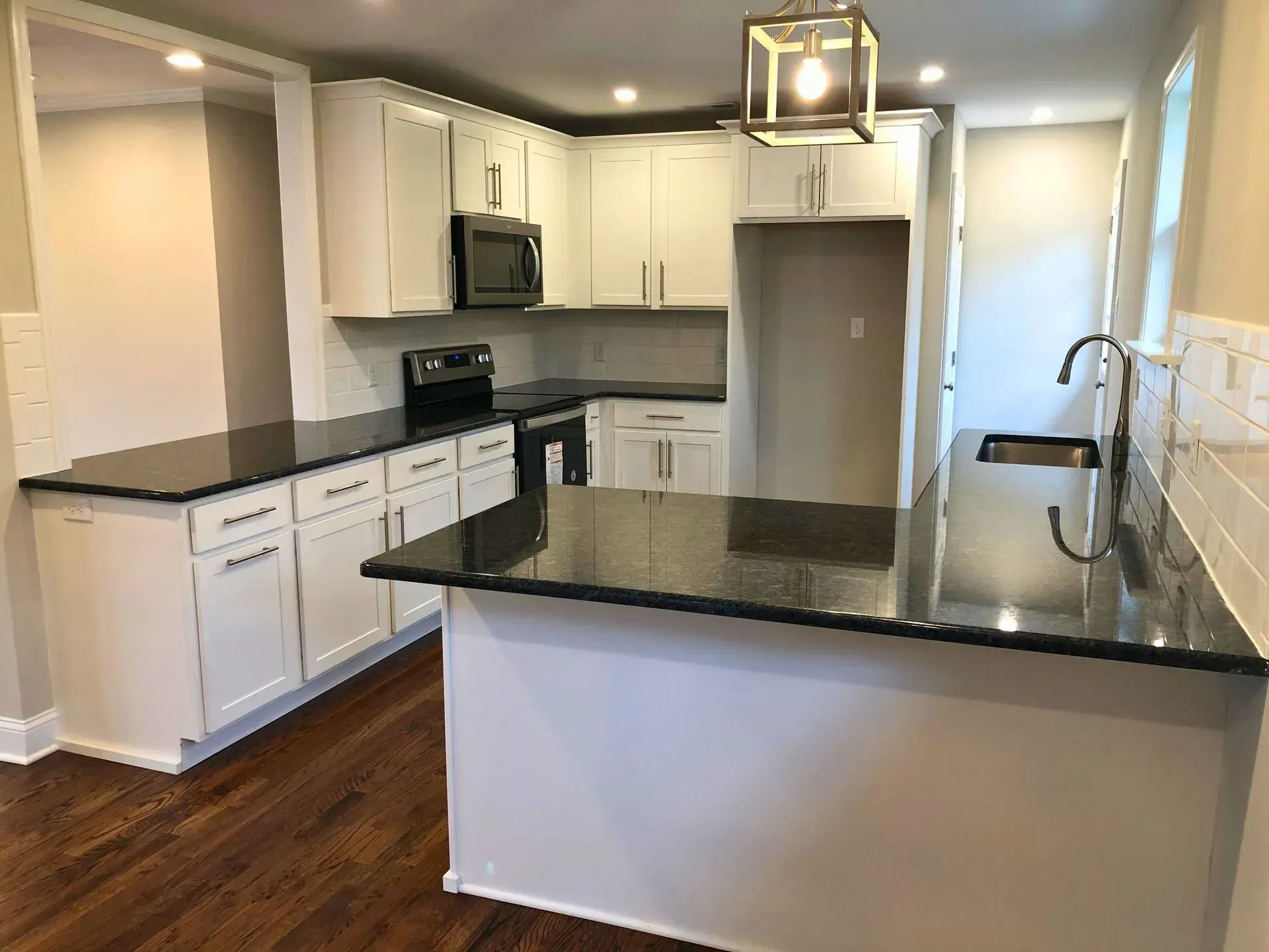 Modern kitchen with white cabinets, black countertops, island, stainless appliances, and hardwood floor