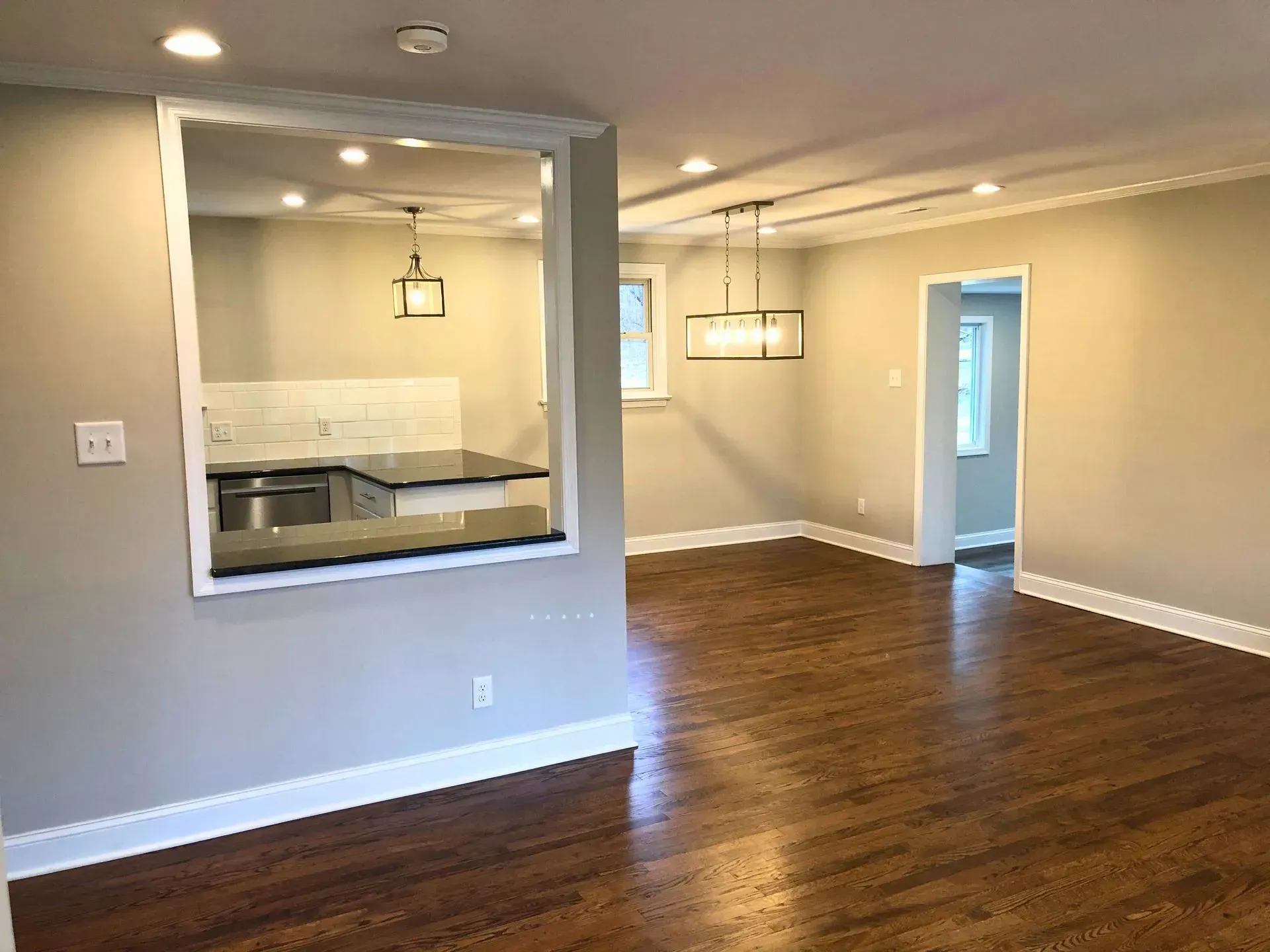 Empty modern living room with hardwood floors, gray walls, and a pass-through window to the kitchen.