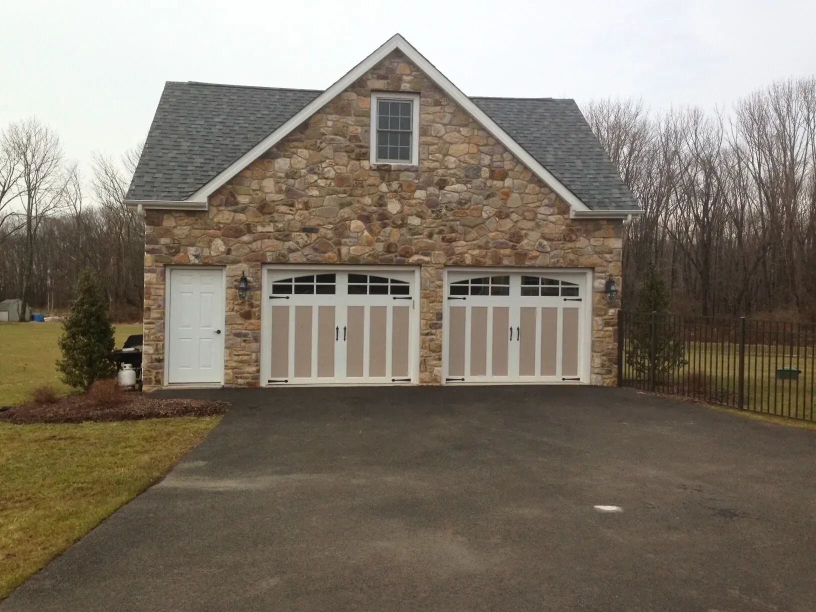 Stone house with three garage doors and a large asphalt driveway, bordered by trees