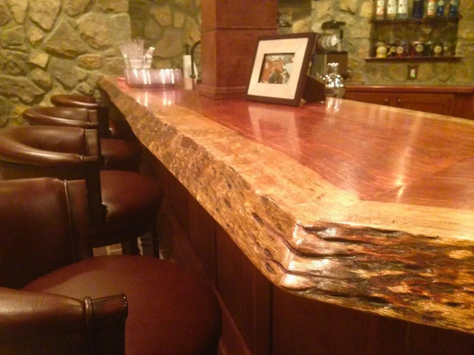 Bar counter with polished marble top, leather stools, and a framed photo in a rustic bar interior