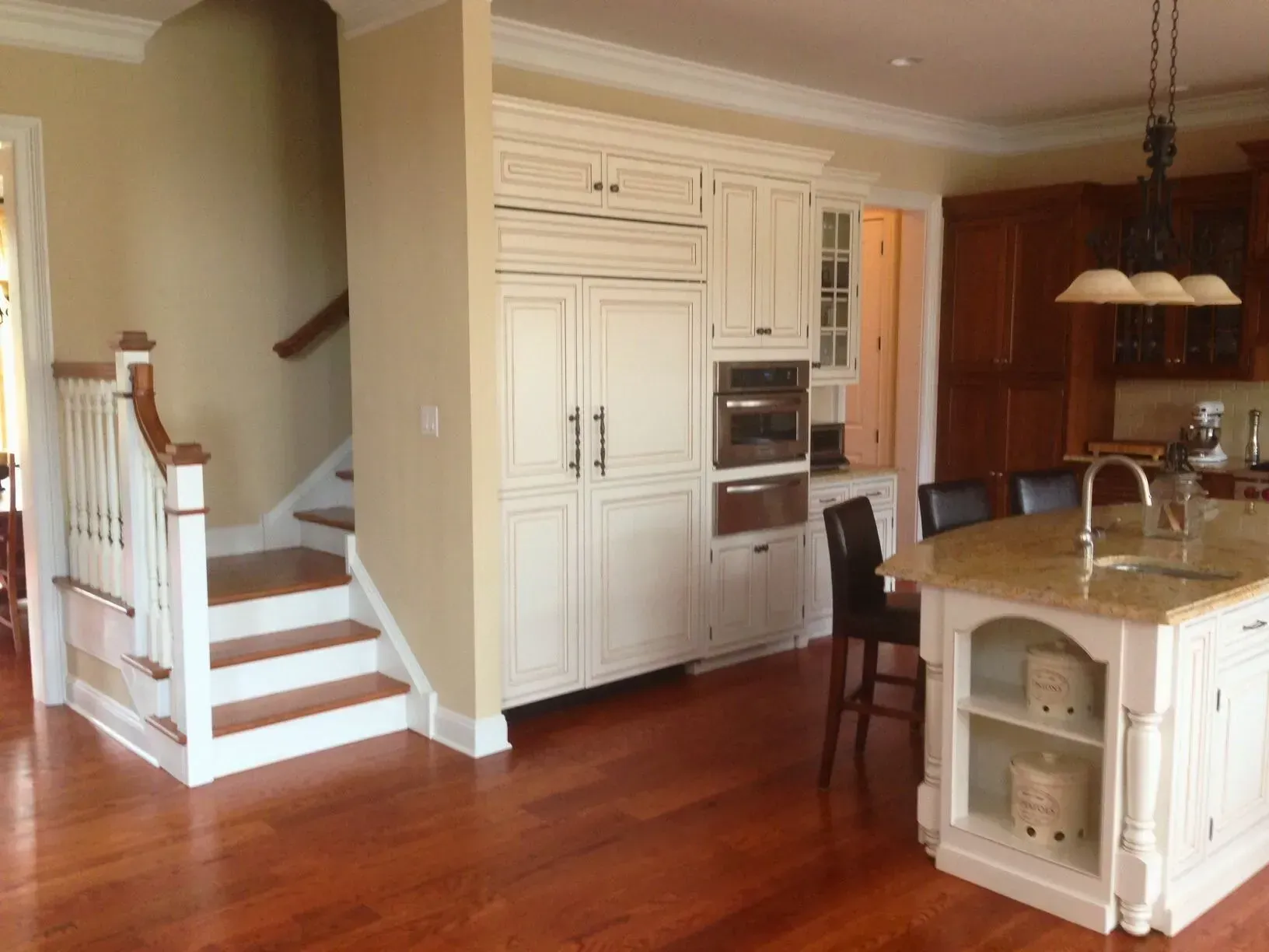Bright kitchen with white cabinets, hardwood floors, island, and stairs leading up on the left