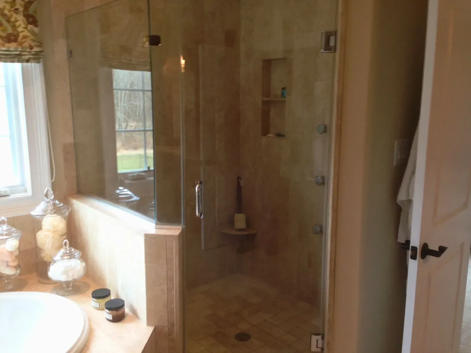 Bathroom with glass-enclosed shower, wooden vanity, and white sink near a window.