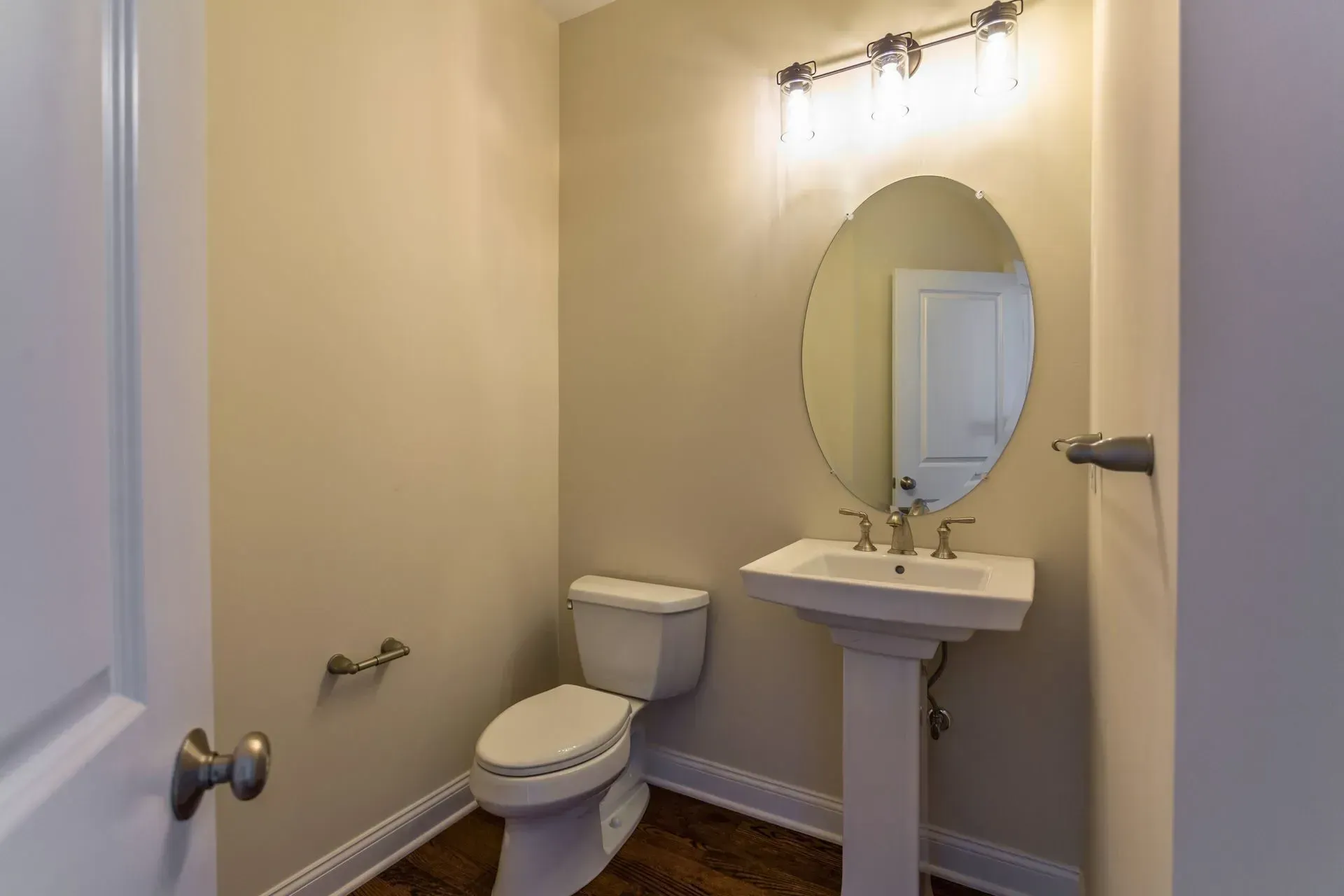 Small beige bathroom with toilet, pedestal sink, mirror, and wall light.