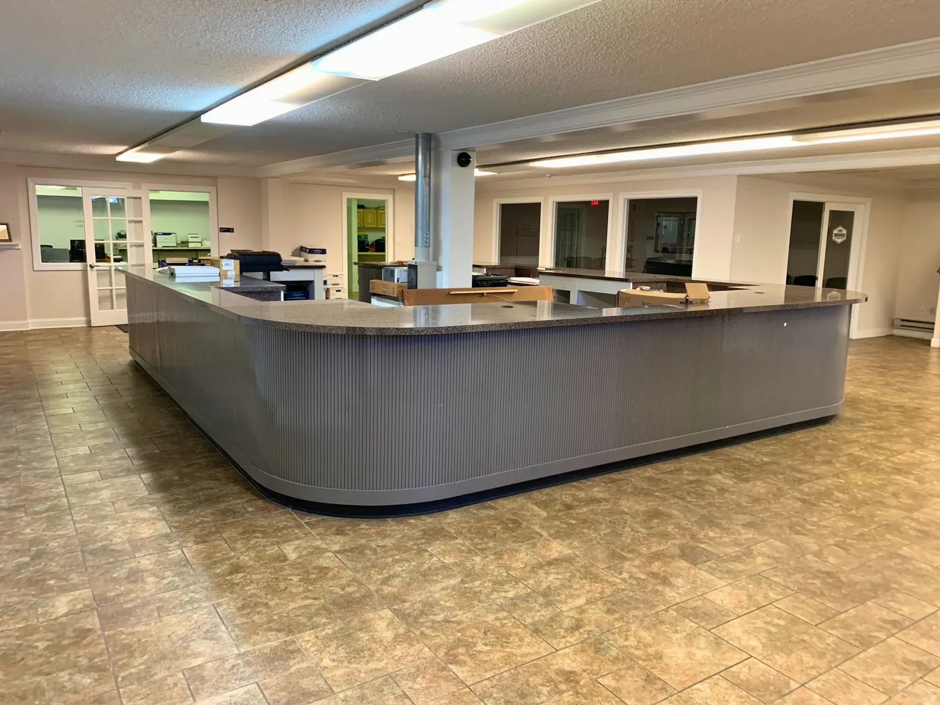 Empty office reception area with a large curved gray desk and beige tiled floor.