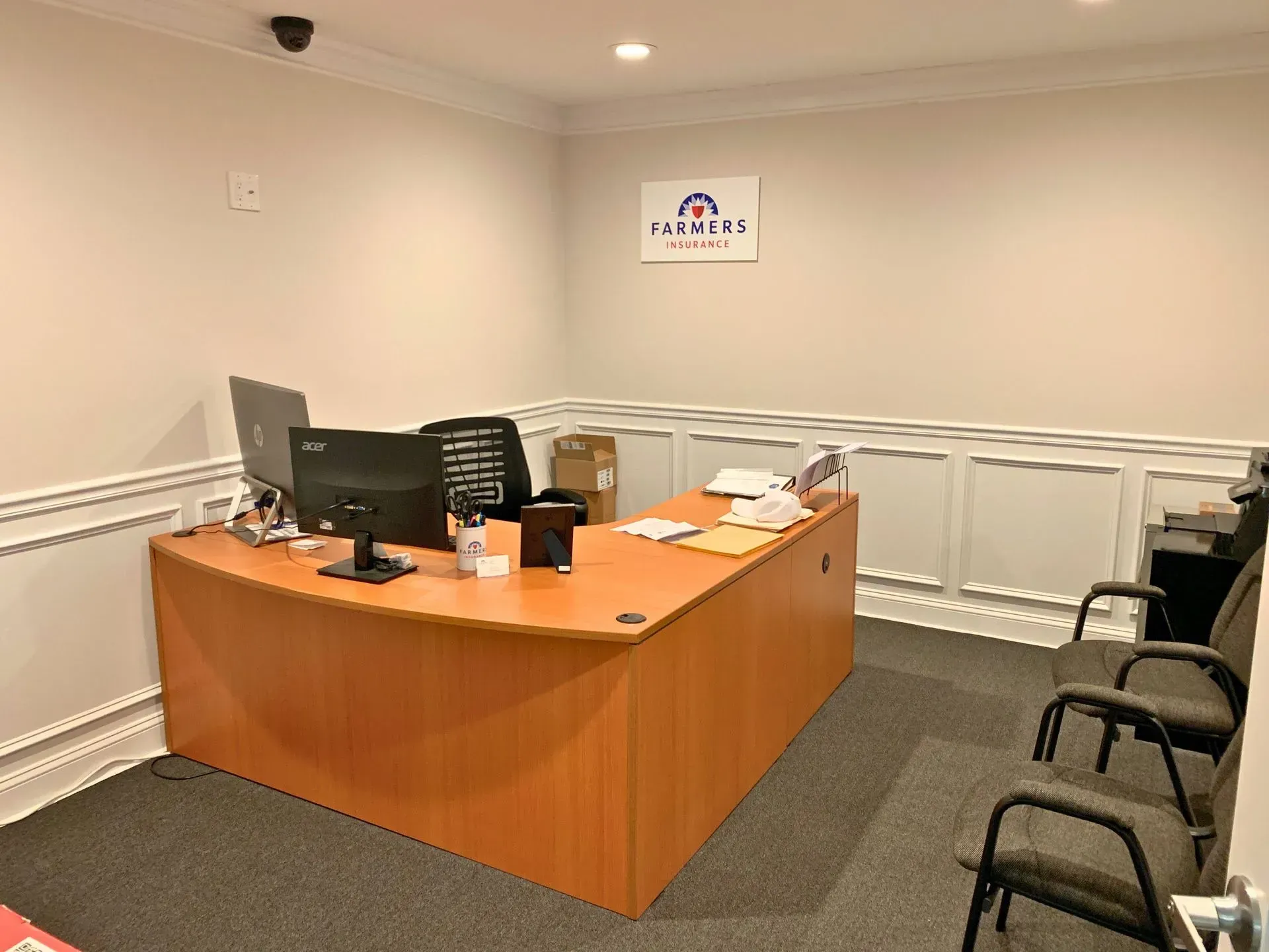 Empty office reception desk with computer, phone, and black chairs in a beige room.