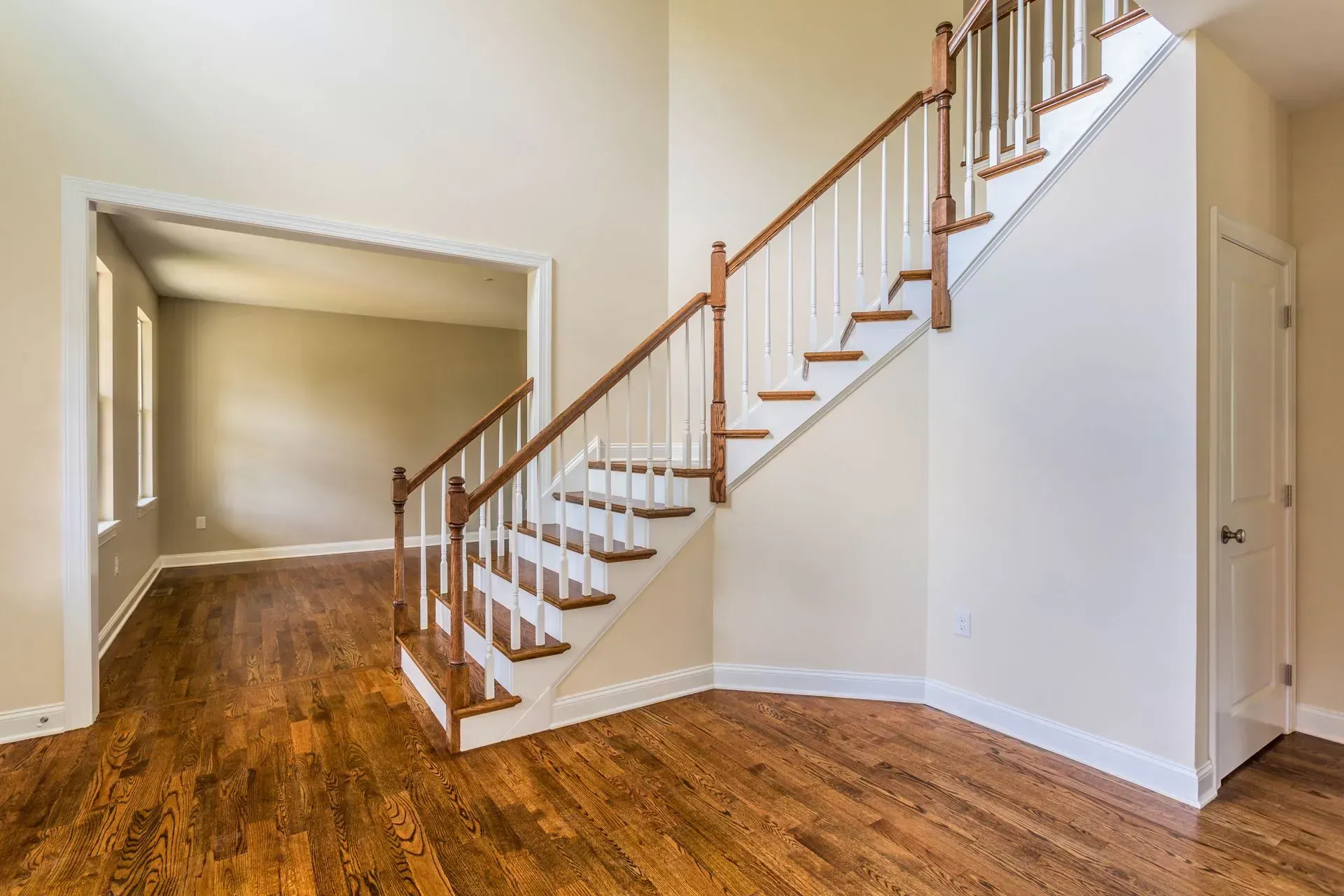 Bright empty room with hardwood floors and a staircase leading up along the right wall