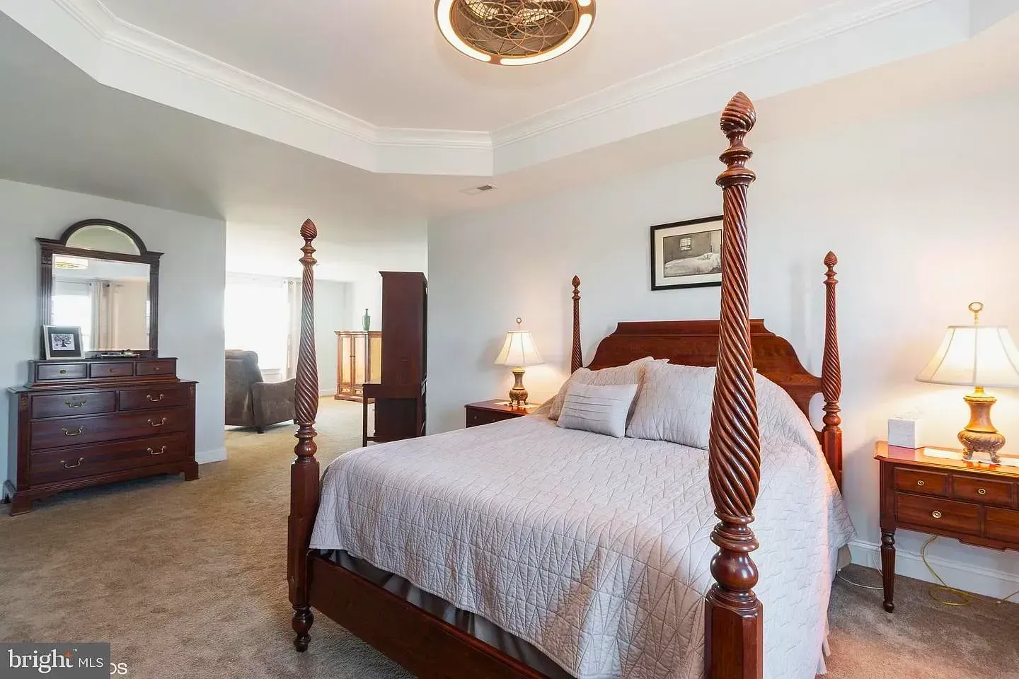 Elegant bedroom with four-poster bed, dresser, nightstands, and beige carpet in a bright, traditional setting