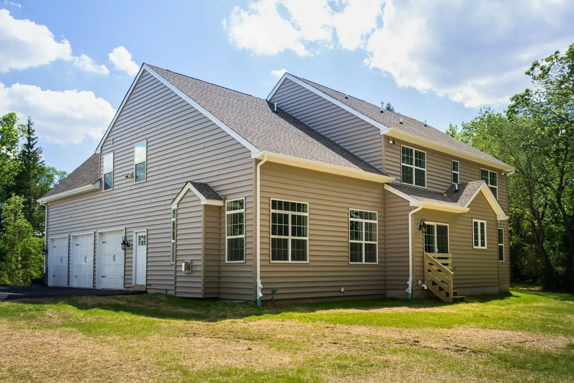 Tan house with white garage doors and a gray roof, viewed from the yard on a sunny day.