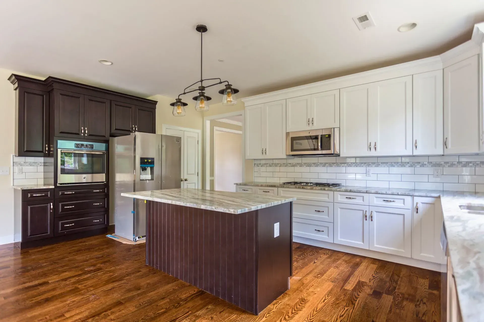 Modern kitchen with white cabinets, dark island, hardwood floors, and stainless steel appliances.