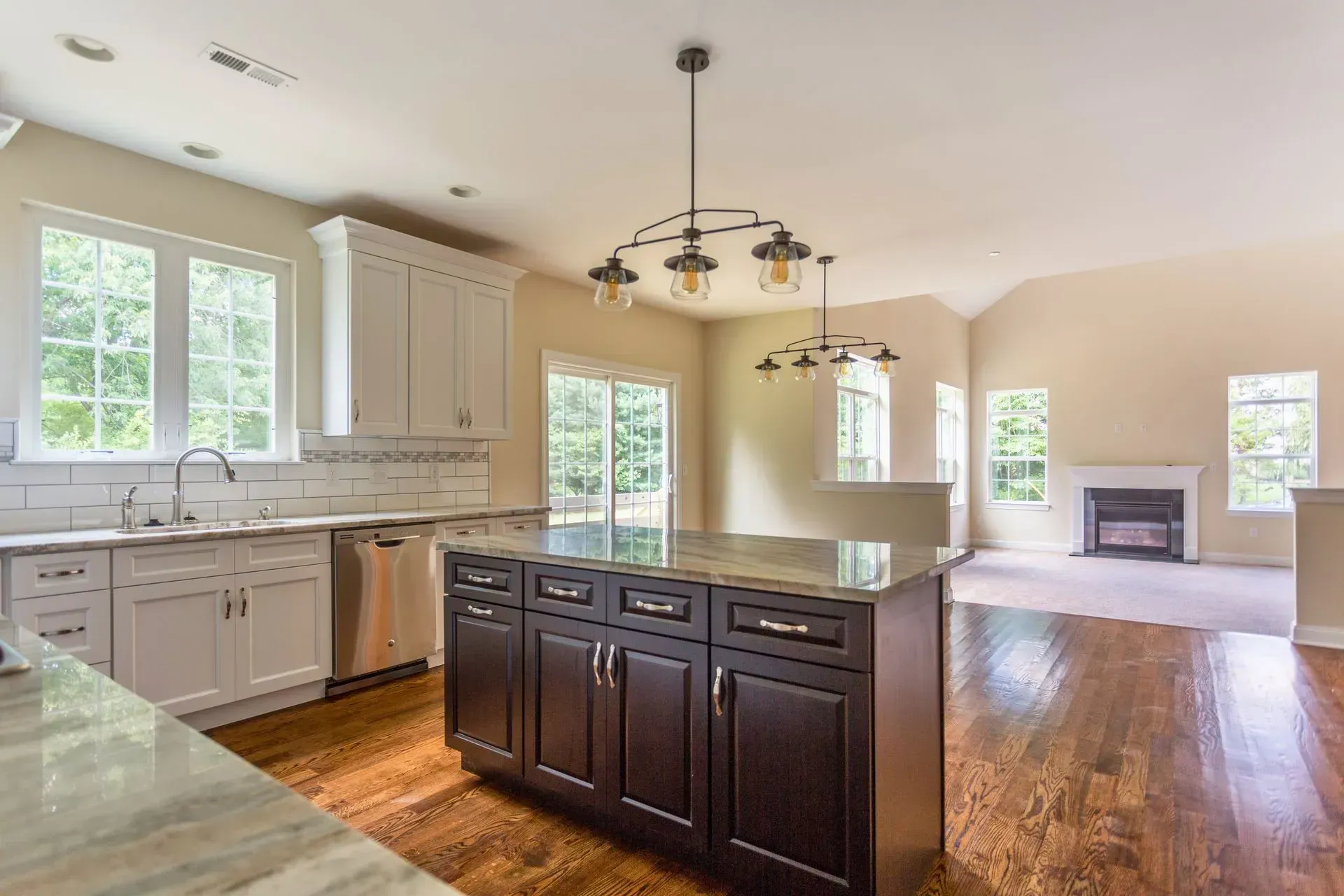 Bright kitchen with white cabinets, dark island, hardwood floors, and open view to living room with fireplace