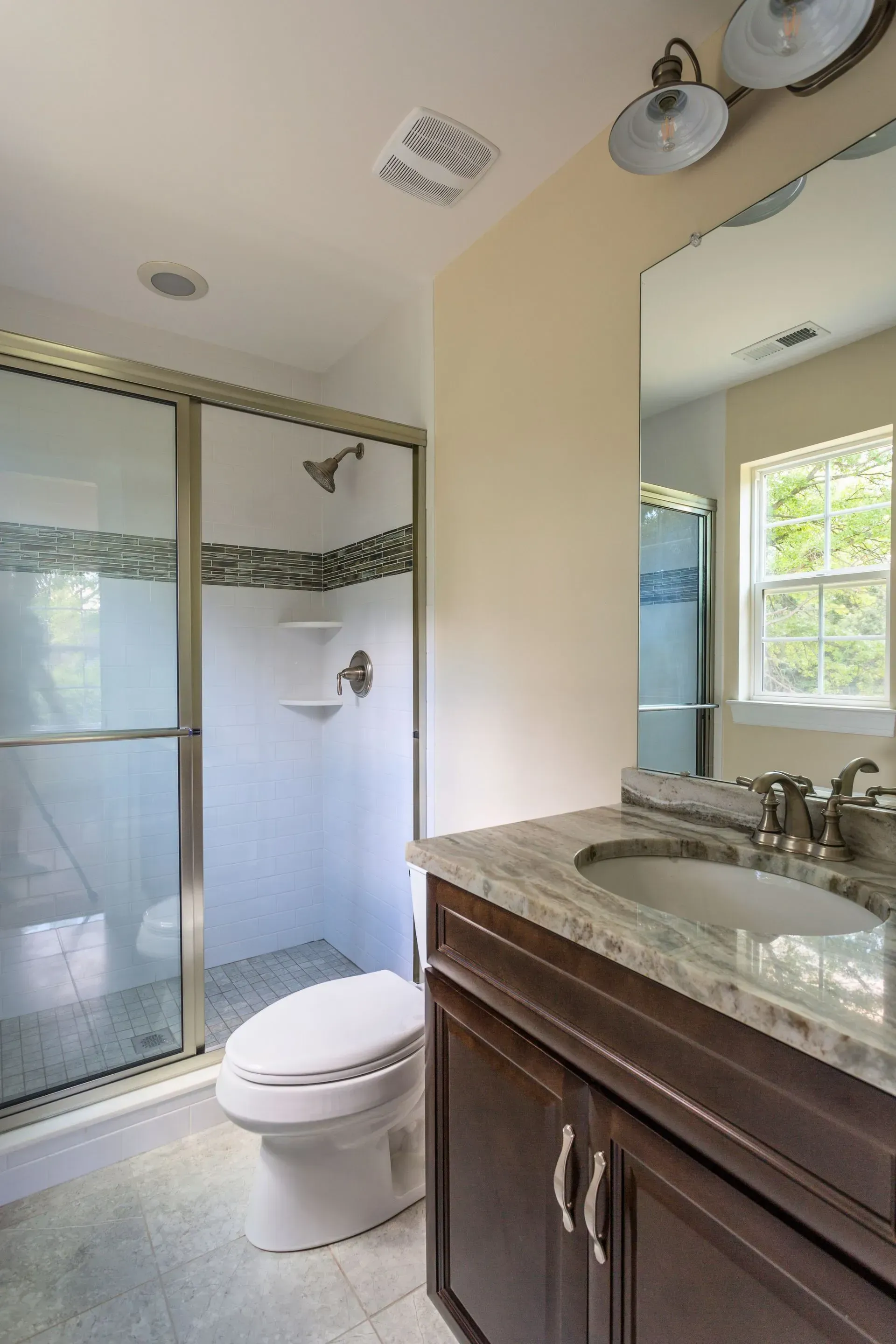 Bathroom with glass shower, toilet, and dark vanity with granite countertop and mirror.