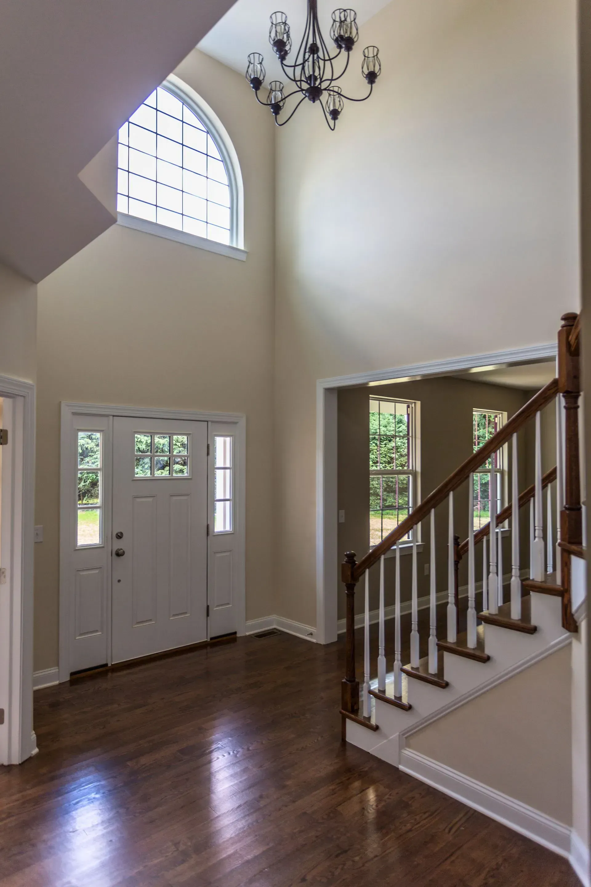 Bright foyer with white double doors, arched window, chandelier, and staircase with wood railing