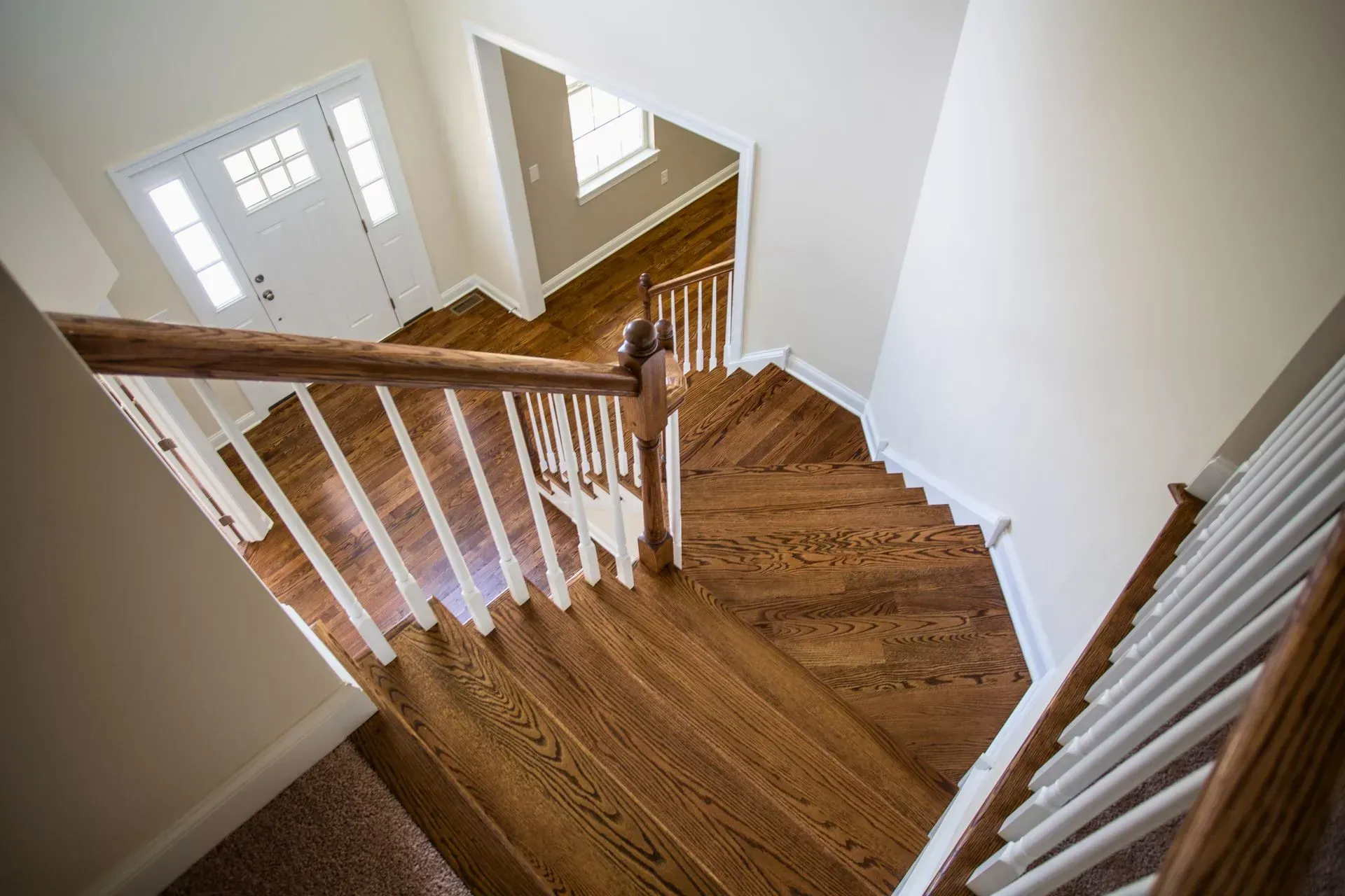 Wooden staircase landing with white railings and a front door in a bright home interior