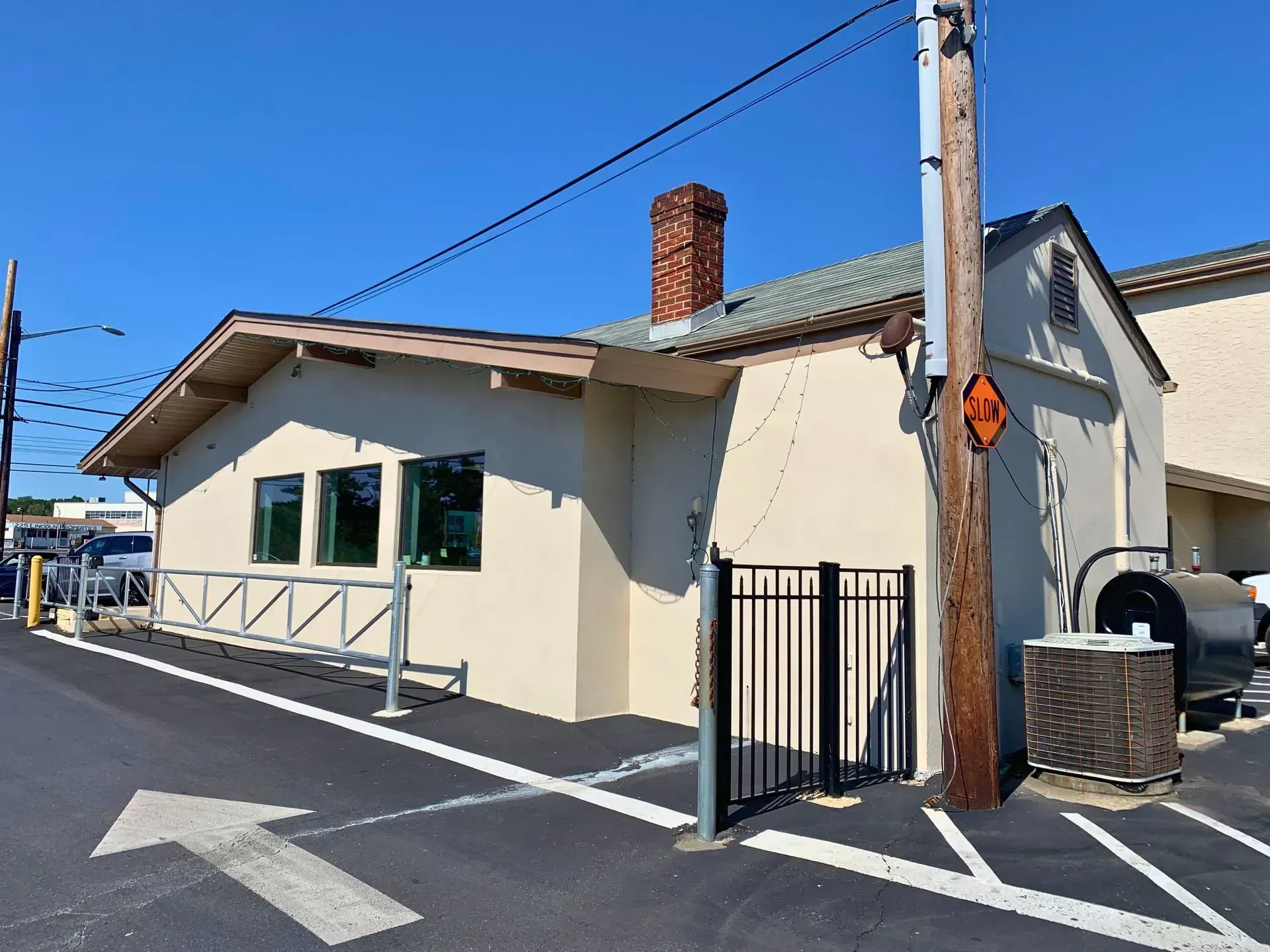 Small cream-colored corner building with a gate and white railing on a sunny street intersection