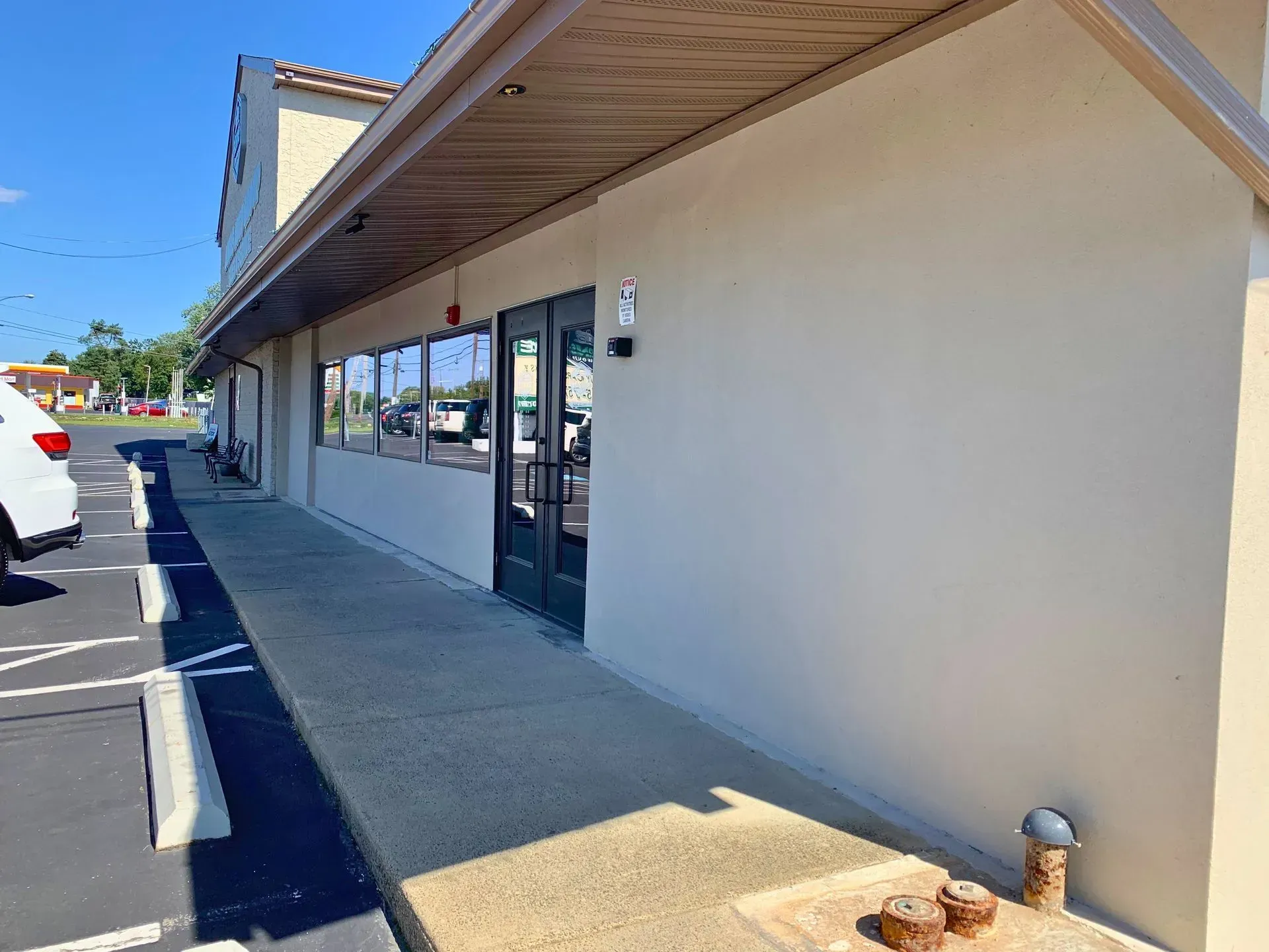Empty storefront walkway with beige wall, glass windows, and parked cars in a strip mall.