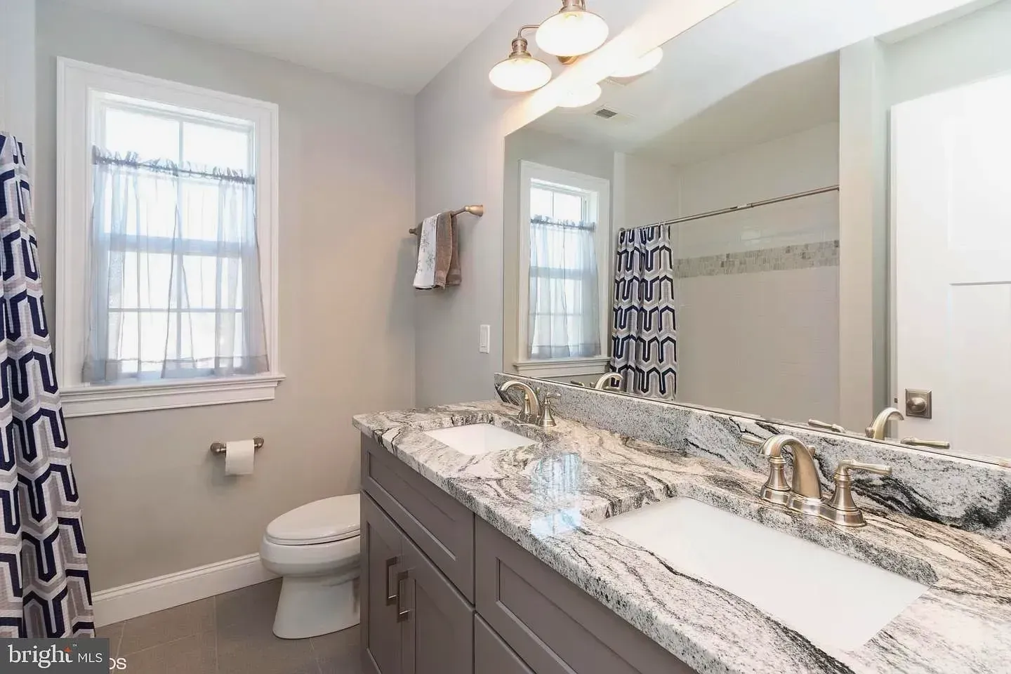 Bright bathroom with double vanity, large mirror, window, shower curtain, and toilet.