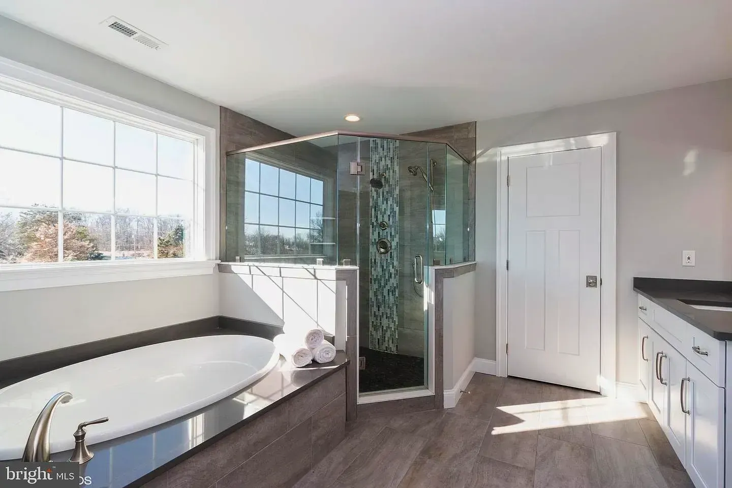Modern bathroom with soaking tub, glass shower, white vanity, and bright window light