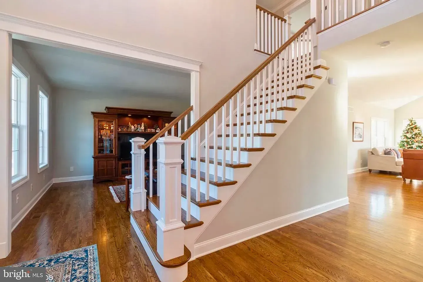 Bright foyer with wooden staircase, hardwood floors, and open view into a dining room and living area