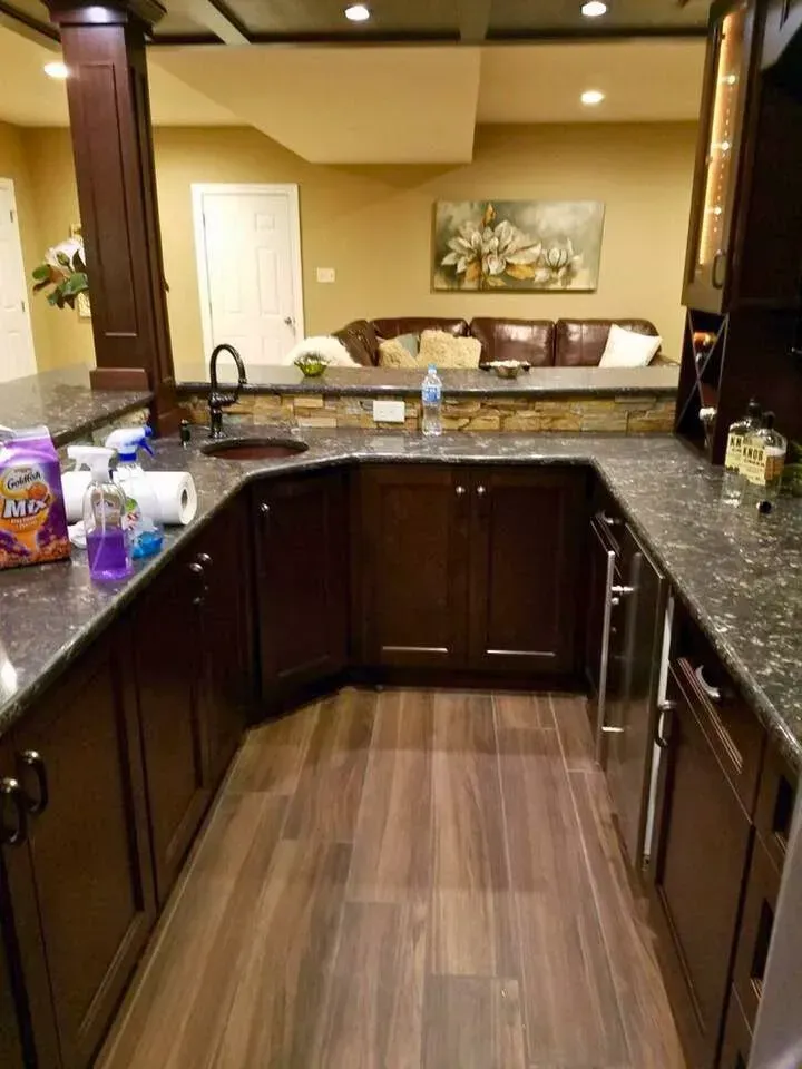 Modern kitchen with dark cabinets, black granite counters, and a view into a living room beyond.