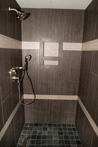 A walk in shower with brown tiles and a shower head.
