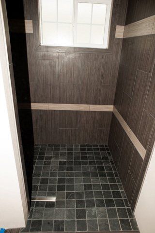 A walk in shower with black tiles and a window.