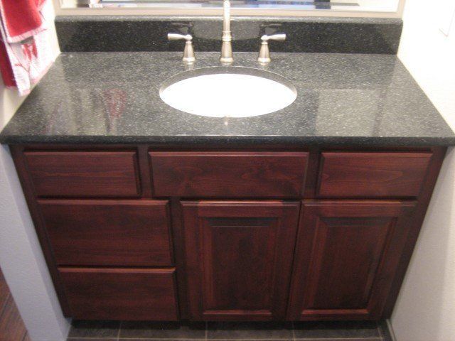 A bathroom vanity with a black counter top and a sink