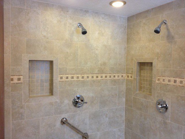 A bathroom shower with two shower heads and a hand rail.