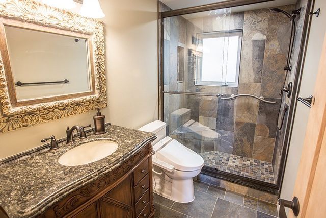 A bathroom with a toilet , sink , mirror and walk in shower.