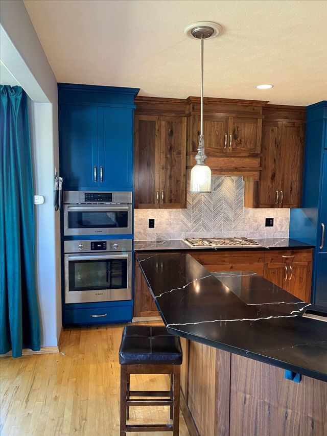 A kitchen with blue cabinets and wooden cabinets and a black counter top.