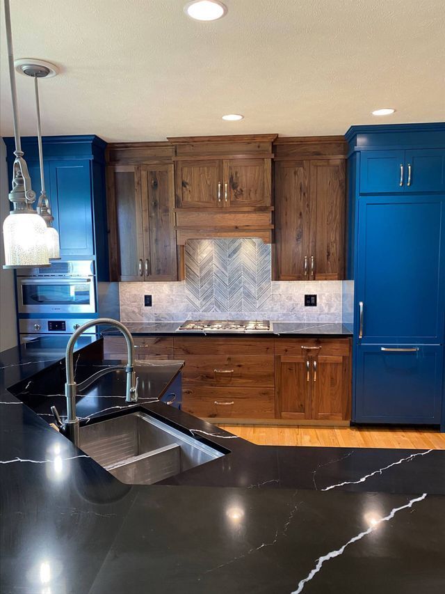 A kitchen with blue cabinets , black counter tops , a sink , and a stove.