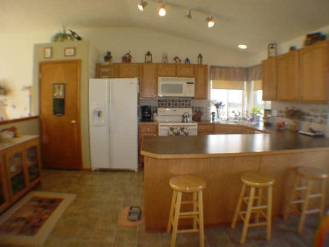 A kitchen with stools and a refrigerator and microwave
